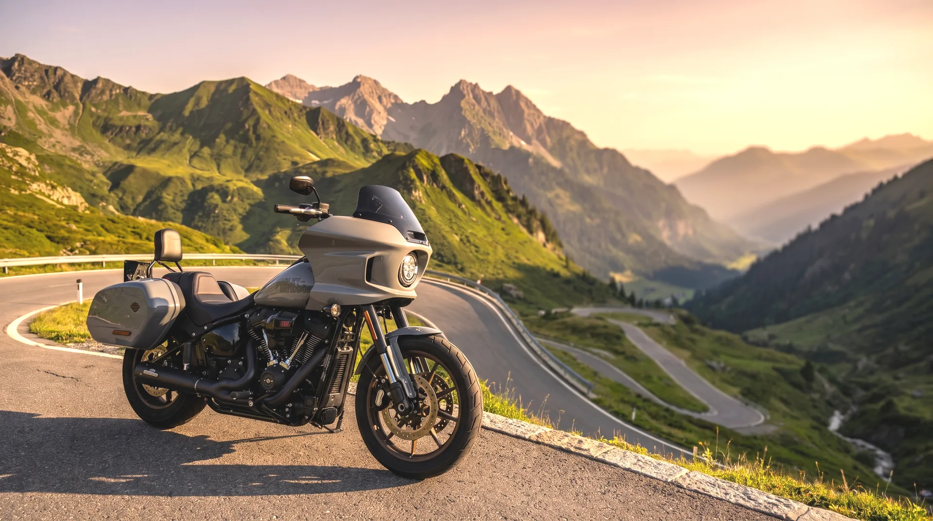 Graue Harley-Davidson Low Rider ST am Rand eines Alpenpasses im Montafon — kurvige Serpentinen und Berggipfel im goldenen Abendlicht